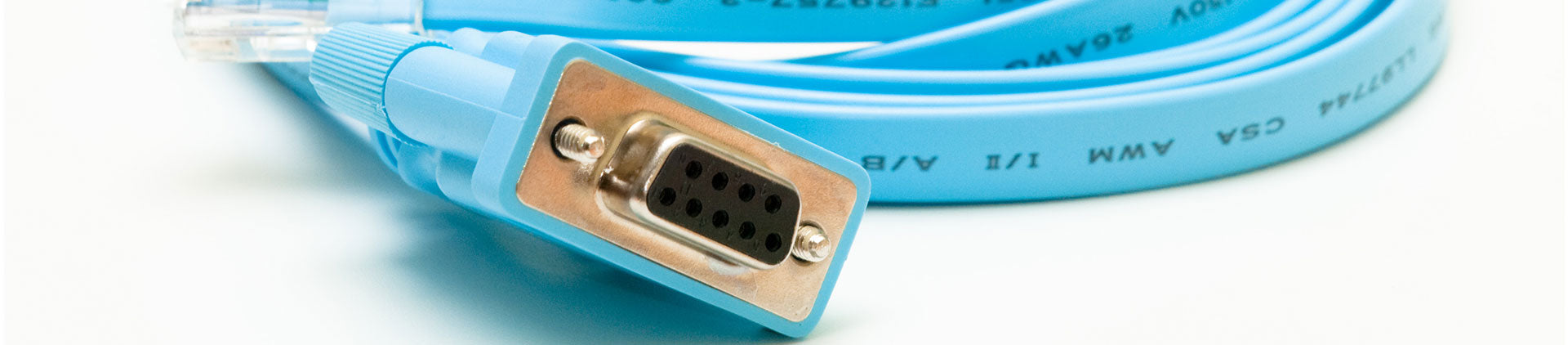 Close-up image of a blue console cable with a DB9 serial connector, featuring clearly visible pins and cable markings, coiled neatly on a white background.