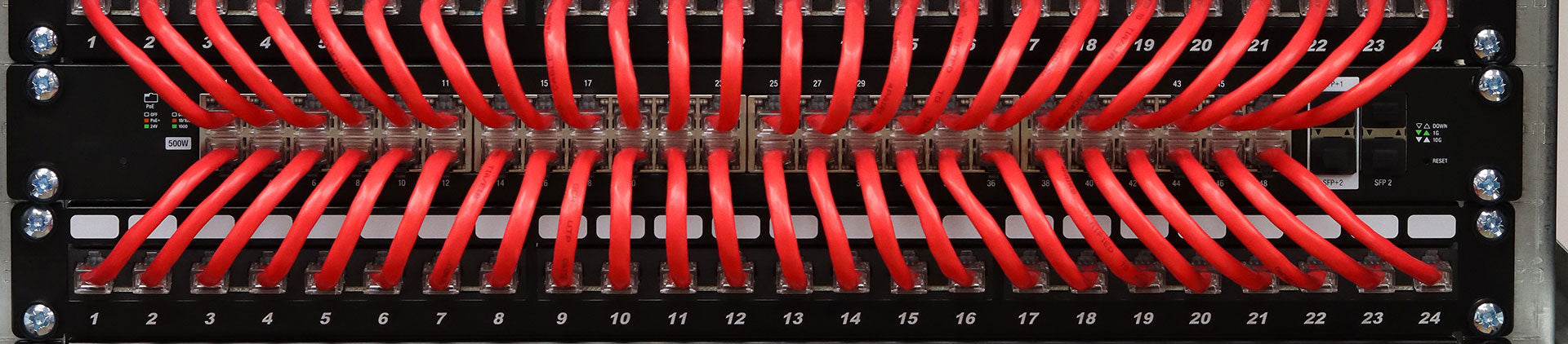 Front-facing image of a network patch panel with multiple red Ethernet cables connected to numbered ports, showcasing a neatly organized and professional network setup.