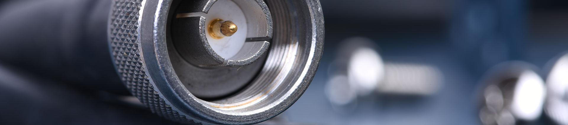 Close-up image of a coaxial cable connector with a threaded metal casing and a visible central pin, showcasing its precision design against a blurred background.