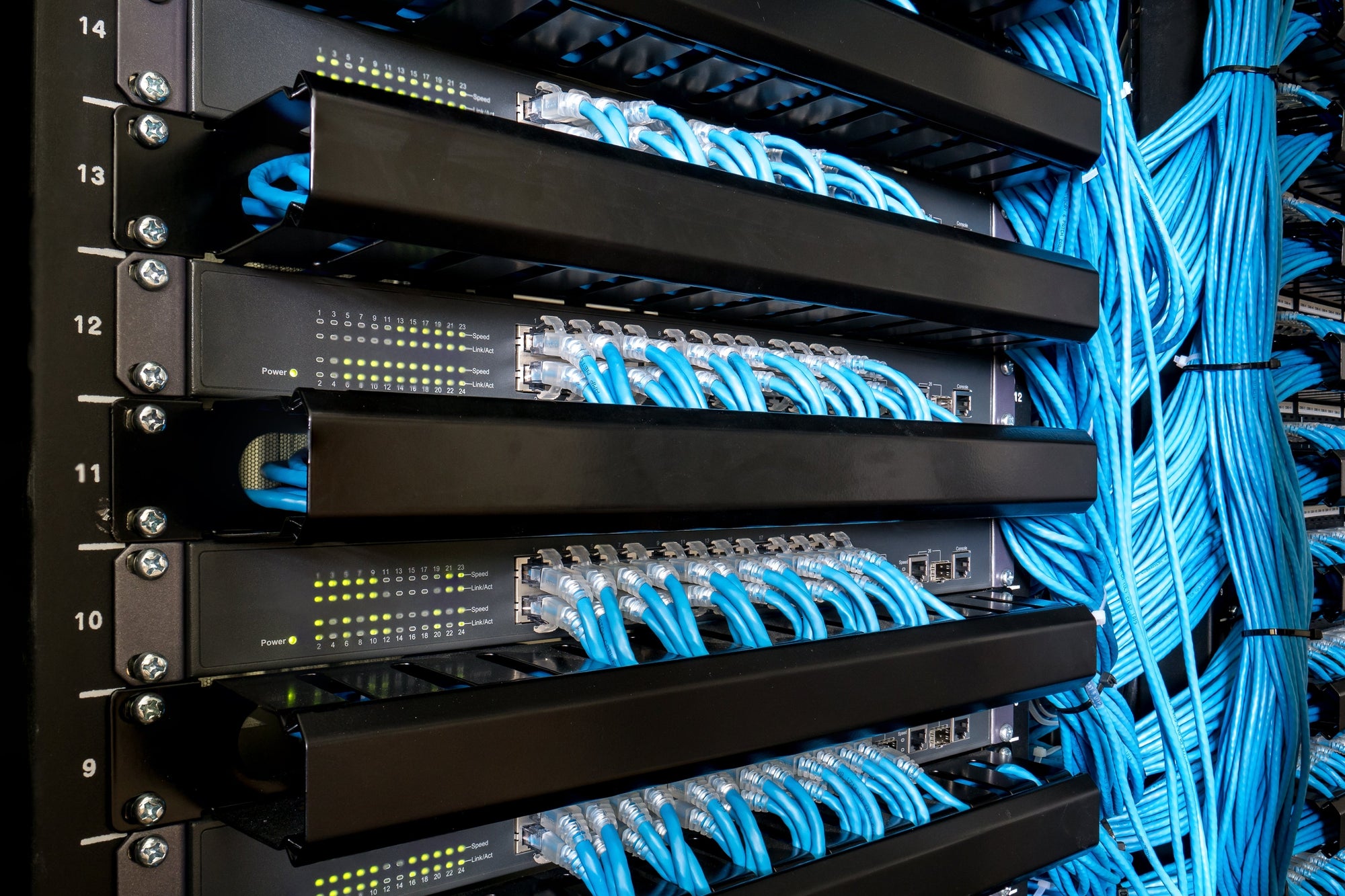 A network rack with several network switches connected with blue network cables.