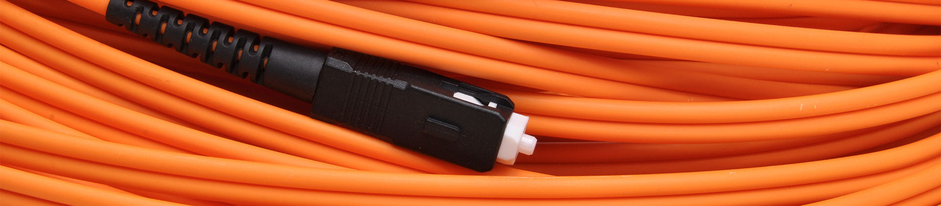 A close-up image of an orange fiber optic patch cable coiled neatly, showcasing its smooth, durable outer sheath and a black connector with a white tip.