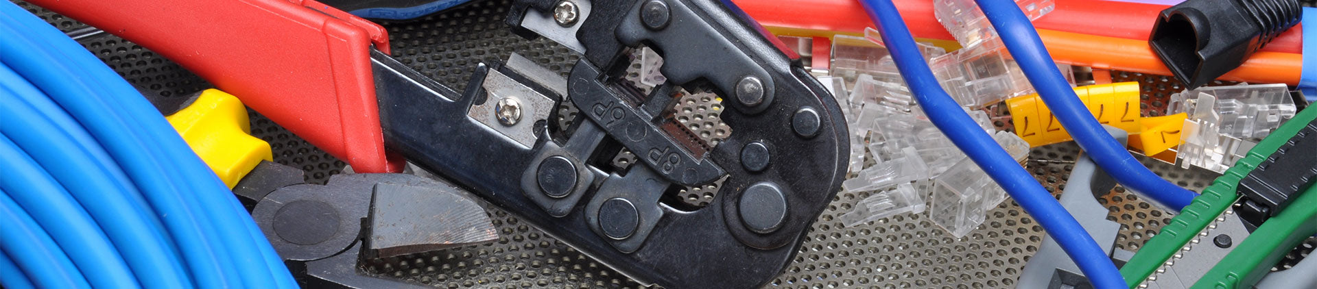 Close-up image of various networking tools and accessories, including a crimping tool, cable cutter, Ethernet cables, connectors, and wire strippers, displayed together on a textured surface.