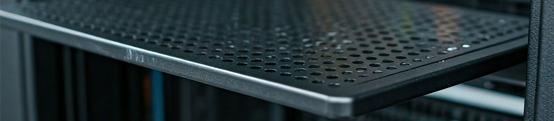 Close-up of a black metal network rack shelf with round perforations, providing ventilation.