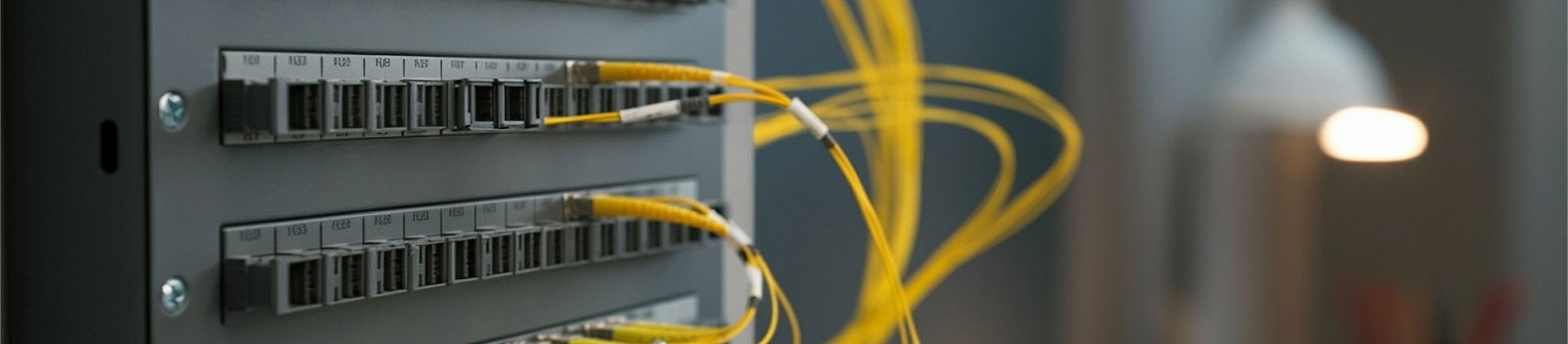 Close-up image of a fiber optic patch panel with multiple yellow fiber optic cables connected, illustrating a clean and organized data networking setup in a modern environment.