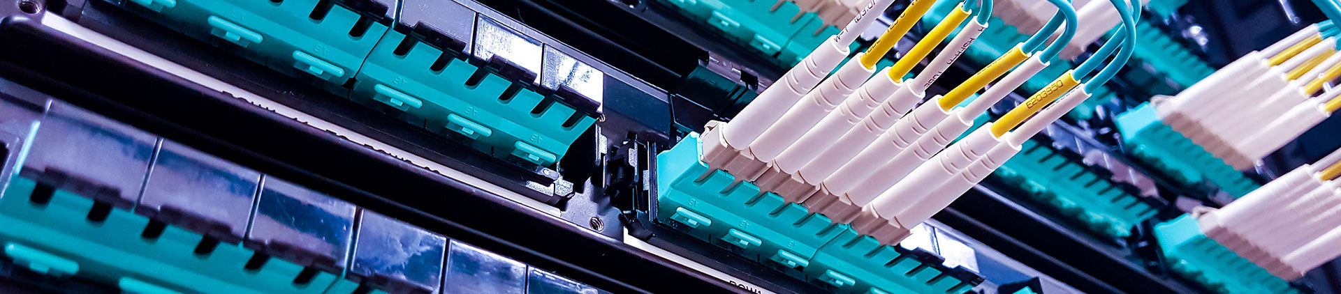 A close-up view of a fiber optic patch panel with loaded connectors and cables, showcasing neatly arranged aqua-colored adapter ports and yellow fiber optic cables.