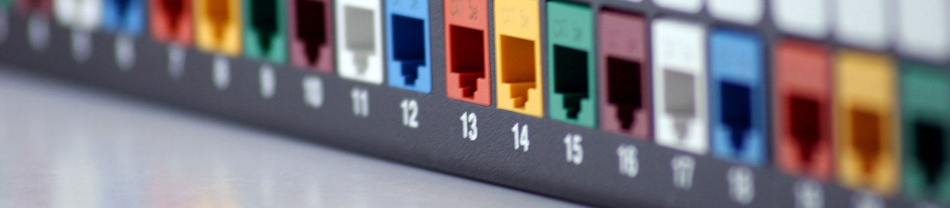 A close-up image of a blank patch panel with colorful keystone jacks arranged in numbered ports.