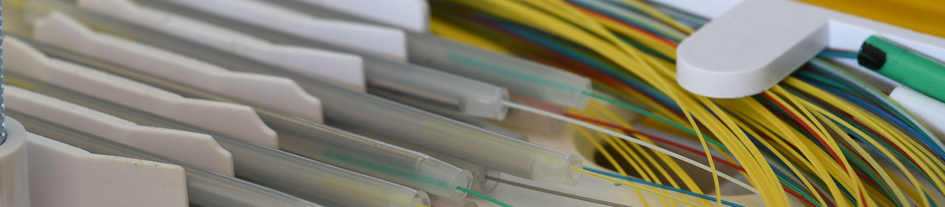 Close-up image of a fiber optic splice tray with organized fiber strands in various colors, along with protective sleeves and connectors, showcasing a detailed view of fiber management.