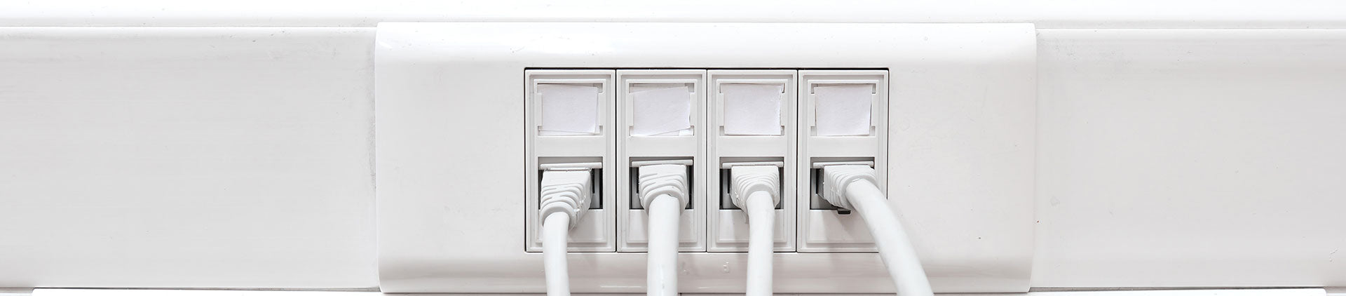Close-up image of a white wall plate with multiple Ethernet ports, each connected with white network cables, illustrating a clean and organized networking setup.