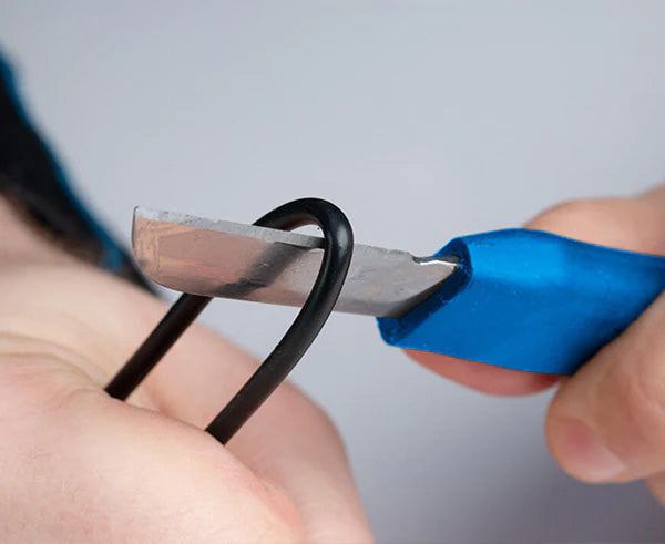 A professional using a sharp tool from the splicer's kit to cut through a black cable