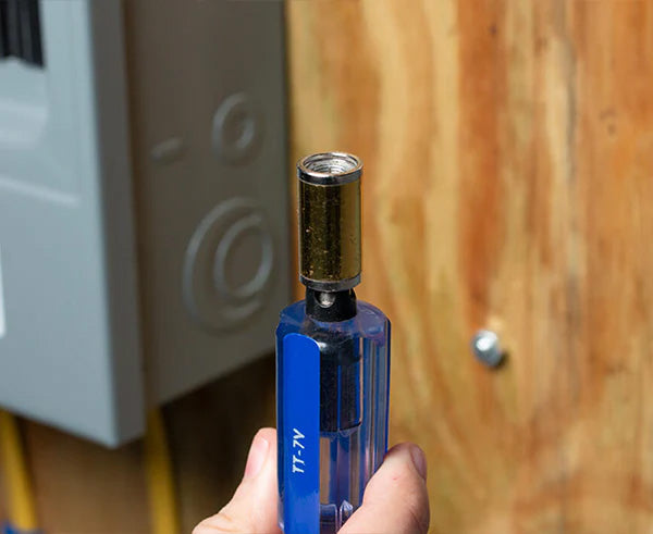 A person holding the 7 1/2" Terminator Tool for PPC and T&B in front of a wooden surface