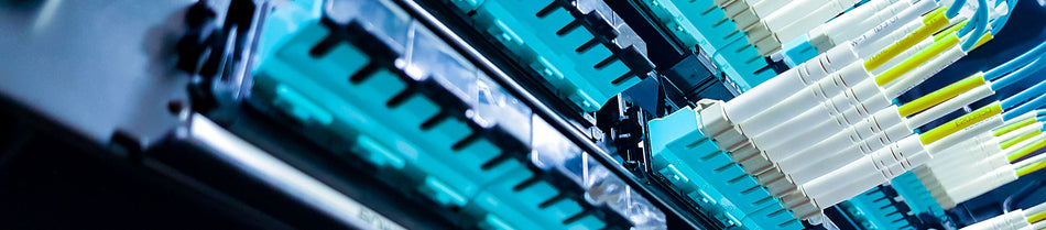 A detailed view of a fiber optic patch panel with OM3 fiber optic cables and connectors. The vibrant aqua-colored cables are neatly organized, emphasizing high-performance networking and advanced connectivity solutions.