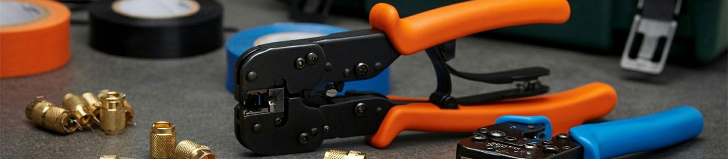 A close-up view of coaxial cable termination tools, including orange and blue-handled crimpers, surrounded by coaxial connectors and rolls of electrical tape.