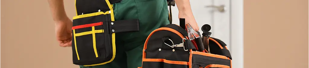 Person carrying a tool bag and wearing a tool belt, showcasing organized and professional storage for tools, set against an indoor background.