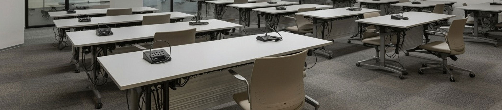 A modern training room featuring multiple rectangular tables on casters, each equipped with a small control device. 