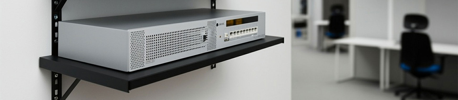 A black metal wall-mounted shelf holding a silver network device with ventilation holes and cable ports.