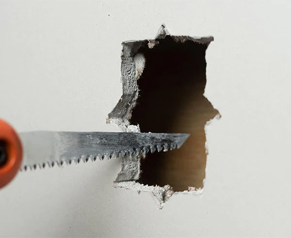 A precise cut being made in drywall with a saw guided by the Wall Box Template