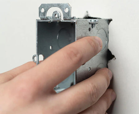 An installer holding a metal electrical box with an attached screw from the Wall Box Template kit