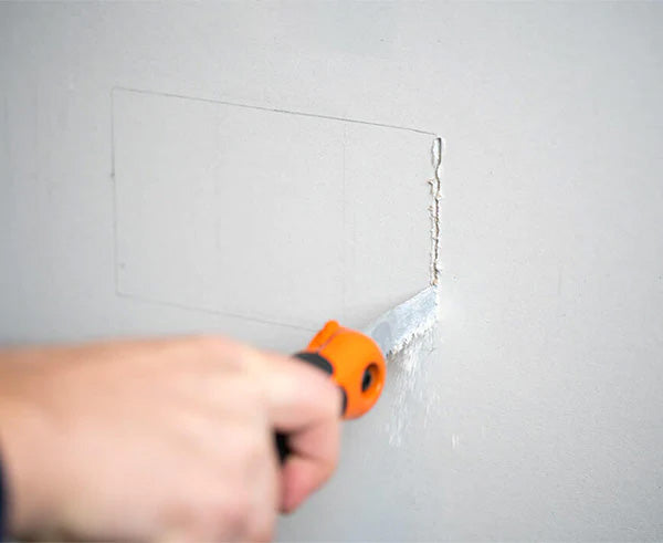 Cutting a precise opening in a wall with a specialized orange cutting tool for box installation